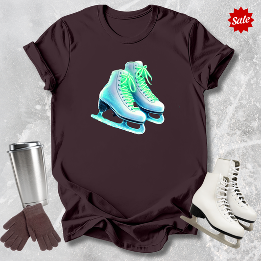 Brown t-shirt with neon ice skate design for figure skaters, silver tumbler, gloves, and white skates on a textured gray background.