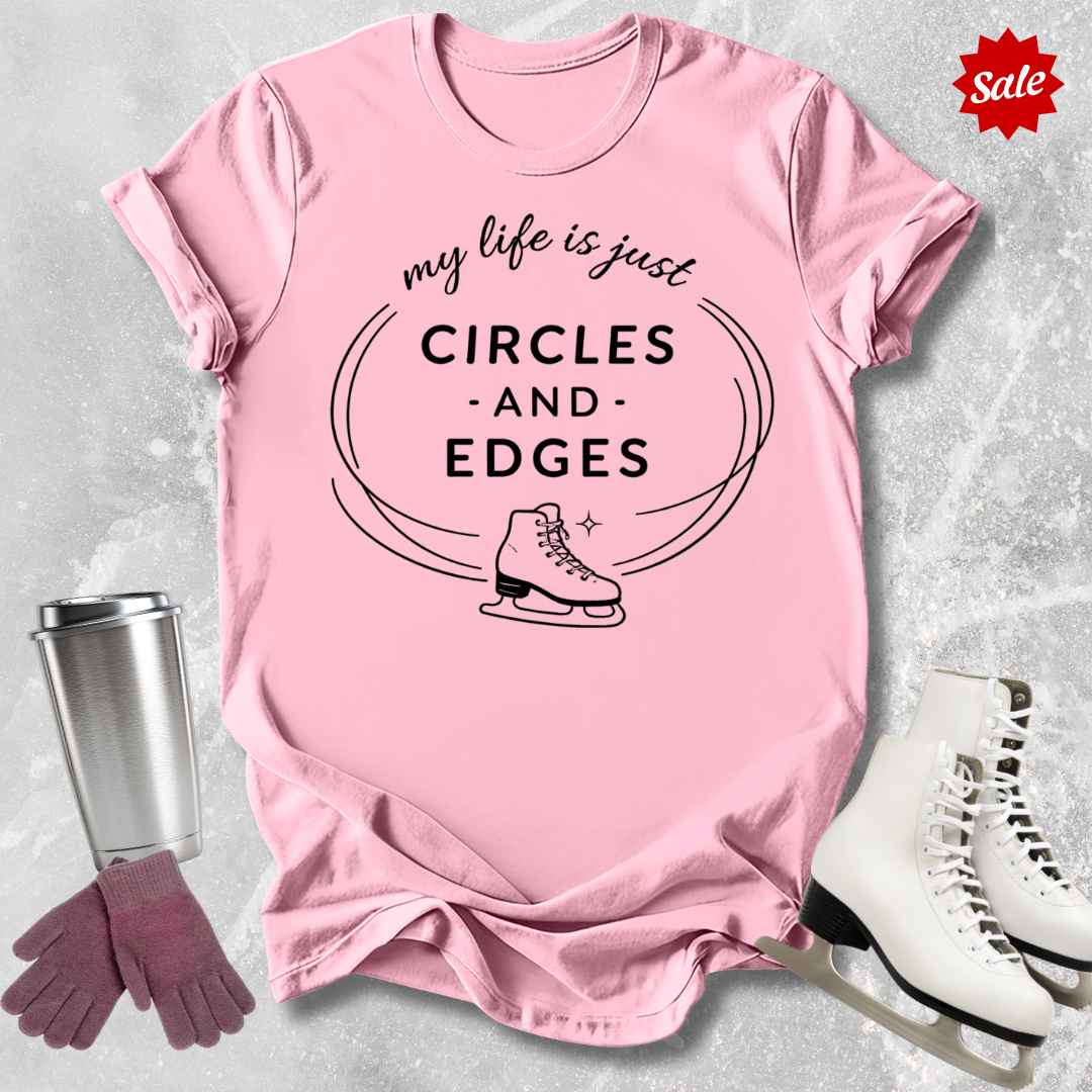 Pink t-shirt with 'my life is just circles and edges' text and ice skates, surrounded by ice skates and a tumbler on a textured surface.