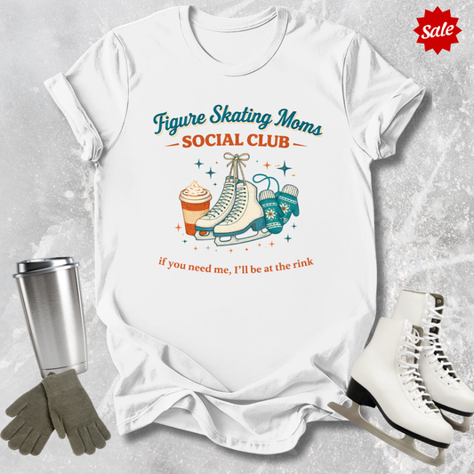 White t-shirt with figure skating-themed design, surrounded by ice skates, gloves, and a tumbler on a textured surface.
