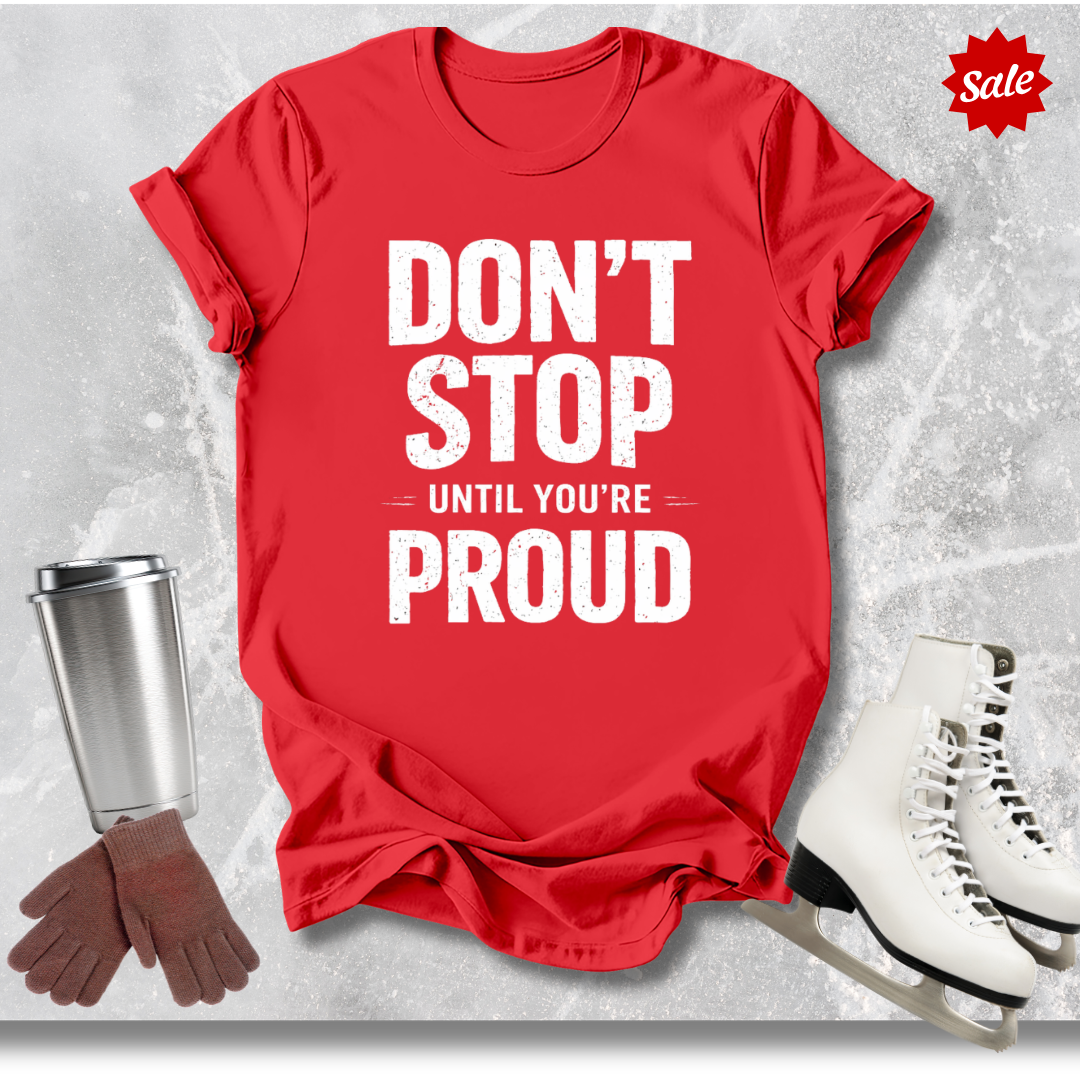 Red t-shirt with 'DON'T STOP UNTIL YOU'RE PROUD' text, next to a silver tumbler, brown gloves, and white skates on a light gray background.