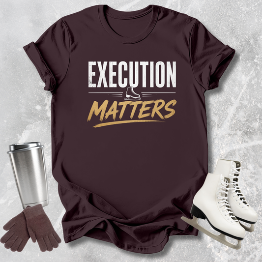Brown t-shirt with 'Execution Matters' text, silver tumbler, brown gloves, and white skates on a textured gray background