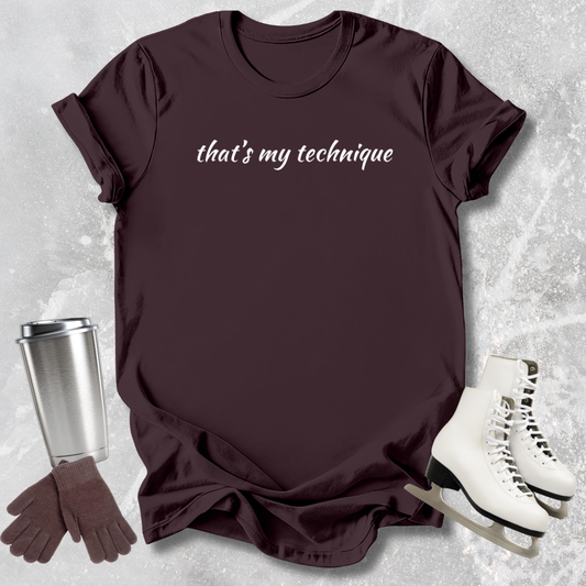Maroon t-shirt with 'that's my technique' text, silver tumbler, brown gloves, and white skates on a textured surface.