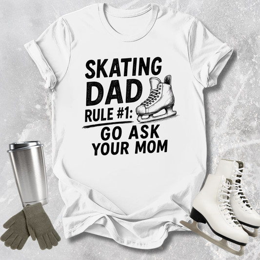 White t-shirt with 'Skating Dad' text, ice skates, gloves, and a tumbler on a gray background