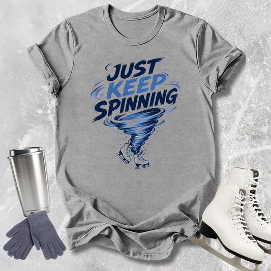 Gray t-shirt with 'Just Keep Spinning' graphic on a textured surface with accessories.