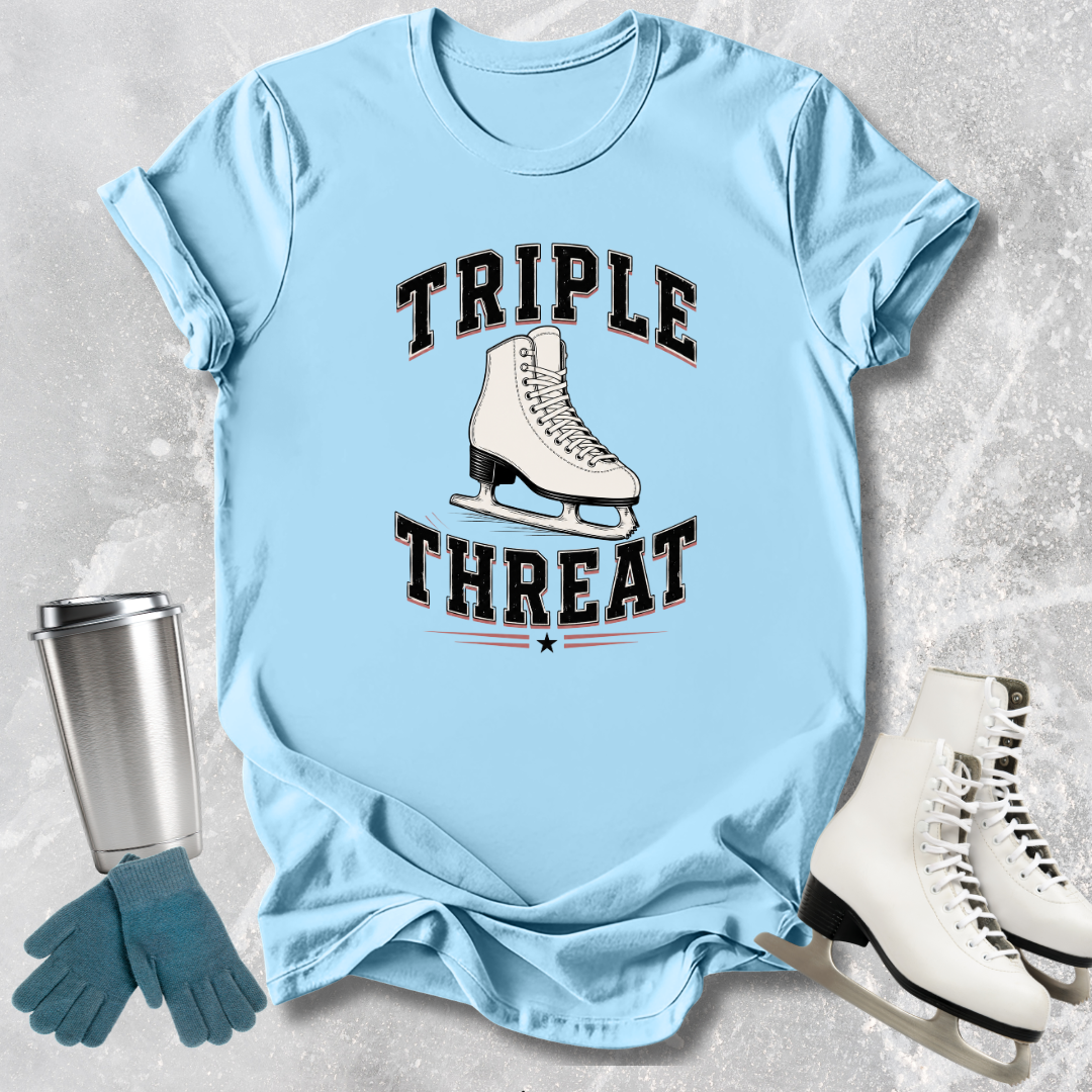 Light blue t-shirt with 'Triple Threat' graphic, next to ice skates and a tumbler on a textured surface.