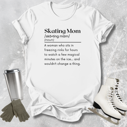 White t-shirt with 'Skating Mom' definition text, surrounded by ice skates, gloves, and a tumbler on a textured surface.
