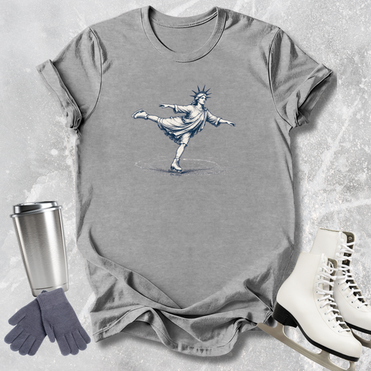 Gray t-shirt with a graphic of the Statue of Liberty, next to a silver tumbler, gray gloves, and white skates on a textured surface.