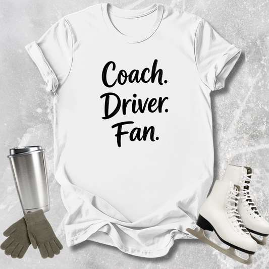White t-shirt with 'Coach. Driver. Fan.' text, surrounded by ice skates, gloves, and a tumbler on a gray background.