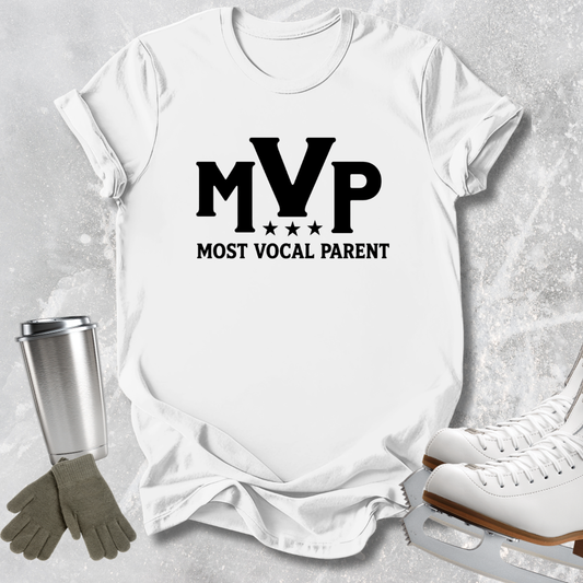 A white short-sleeve T-shirt laid flat on a light textured background, printed with large black 'MVP' lettering and the phrase 'MOST VOCAL PARENT' beneath it. A stainless steel tumbler, gray gloves, and white ice skates are placed around the shirt as styled props.