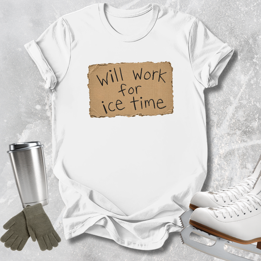 A white short-sleeve T-shirt laid flat on a light gray textured surface, featuring a tan torn-paper style graphic with the phrase 'Will Work for Ice Time' in black script. A stainless steel travel mug, gray gloves, and white ice skates are arranged around the shirt as styled props.