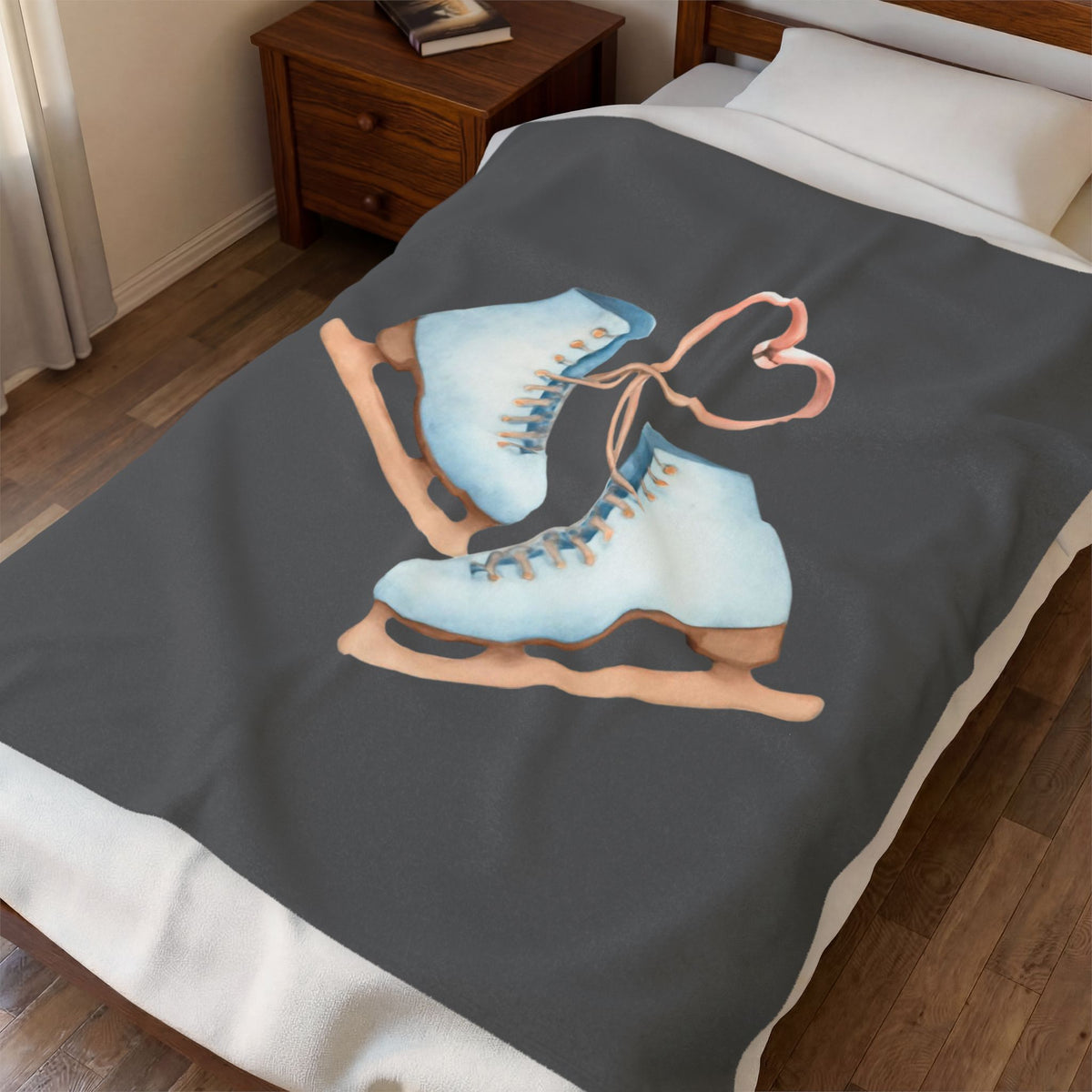 A dark gray blanket featuring a graphic of two light blue ice skates with a pink heart-shaped bow, shown on a bed in a bedroom setting.