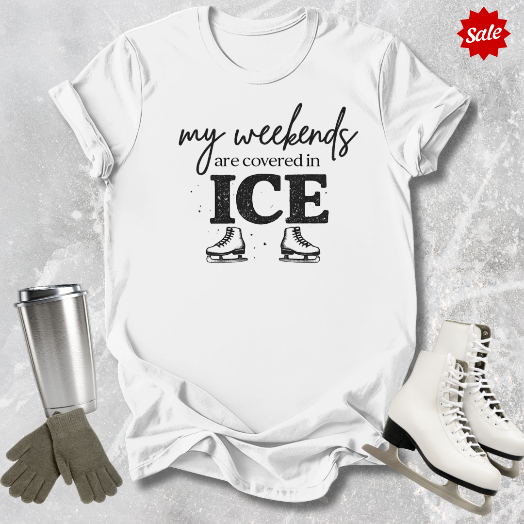 White t-shirt with 'my weekends are covered in ICE' text, surrounded by ice skates and a tumbler on a textured surface.