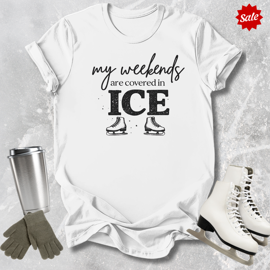 White t-shirt with 'my weekends are covered in ICE' text, surrounded by ice skates and a tumbler on a textured surface.
