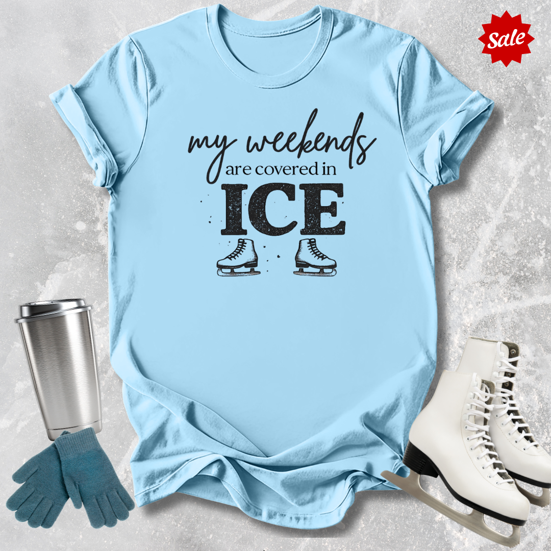 Light blue t-shirt with 'my weekends are covered in ICE' text, surrounded by ice skates, gloves, and a tumbler on a textured surface.
