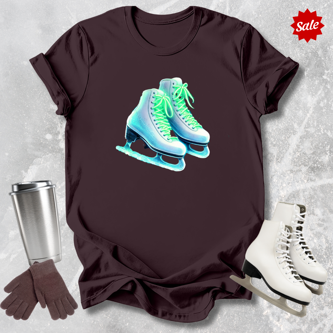 Brown t-shirt with neon ice skate design  for figure skaters, silver tumbler, gloves, and white skates on a textured gray background.