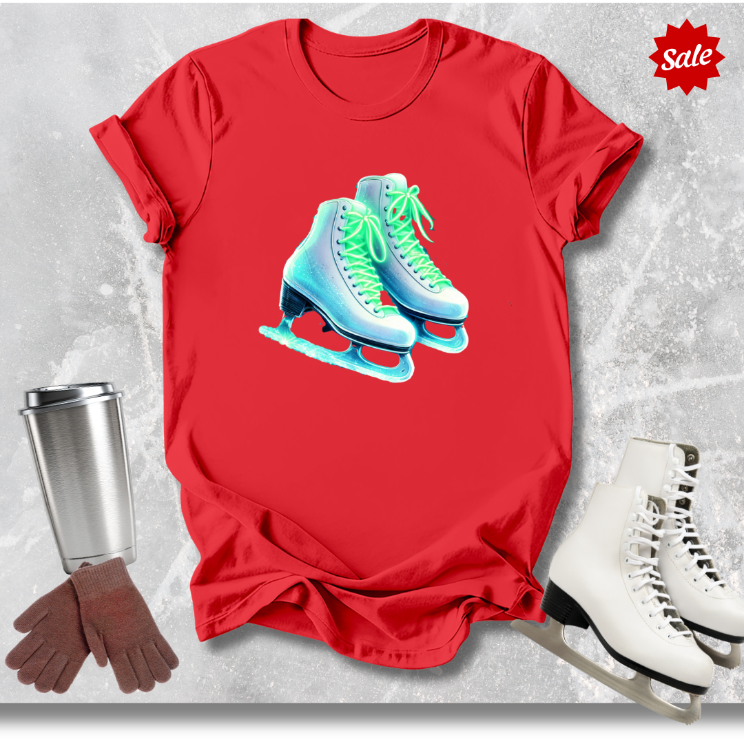 Red t-shirt with neon ice skates graphic  for figure skaters, silver tumbler, brown gloves, and white ice skates on a textured gray background.