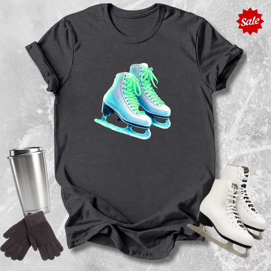 Black t-shirt with neon ice skate design  for figure skaters, silver tumbler, black gloves, and white ice skates on a textured gray background.