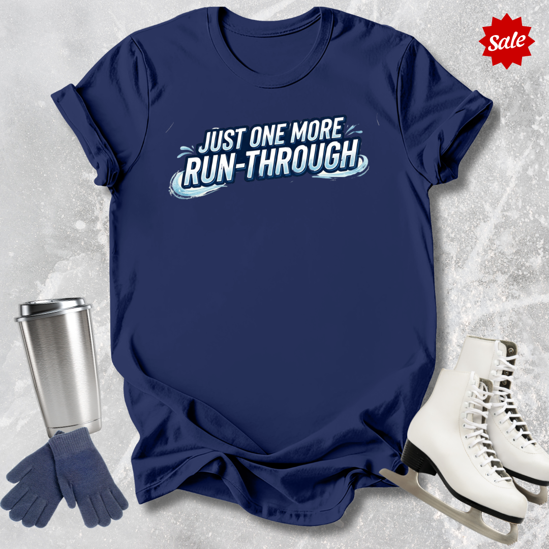 Navy blue t-shirt with 'Just One More Run-Through' text  for figure skaters, next to ice skates and a tumbler on a textured gray background.