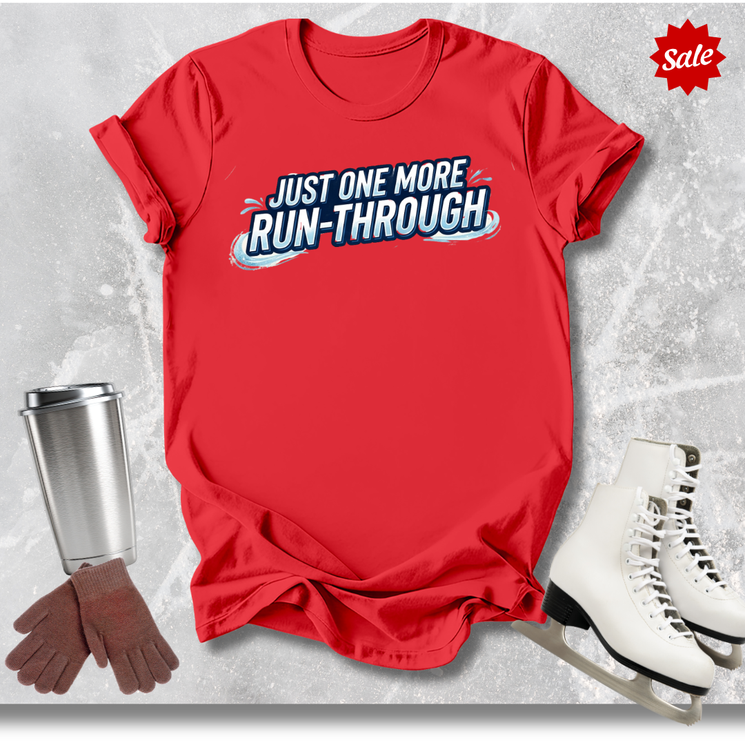 Red t-shirt with 'Just One More Run-Through' text  for figure skaters, next to ice skates, gloves, and a cup on a textured gray background.