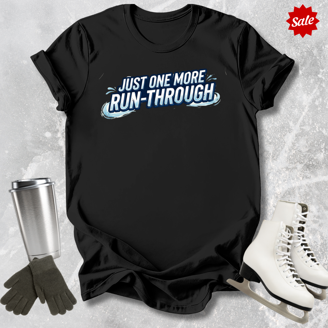 Black t-shirt with 'Just One More Run-Through' text  for figure skaters, placed on a textured surface with ice skates and gloves.