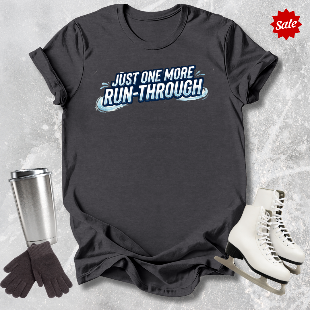 Dark gray t-shirt with 'Just One More Run-Through' text  for figure skaters, surrounded by ice skates, gloves, and a travel mug on a textured ice background.