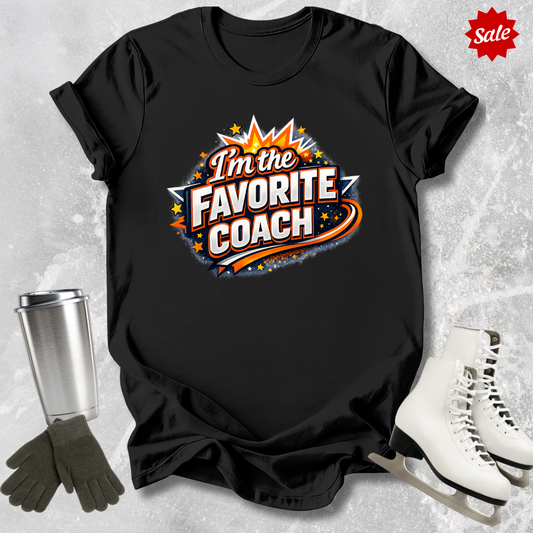 Black t-shirt with 'I'm the Favorite Coach' design  for figure skating coaches on a textured gray background with ice skates and gloves.