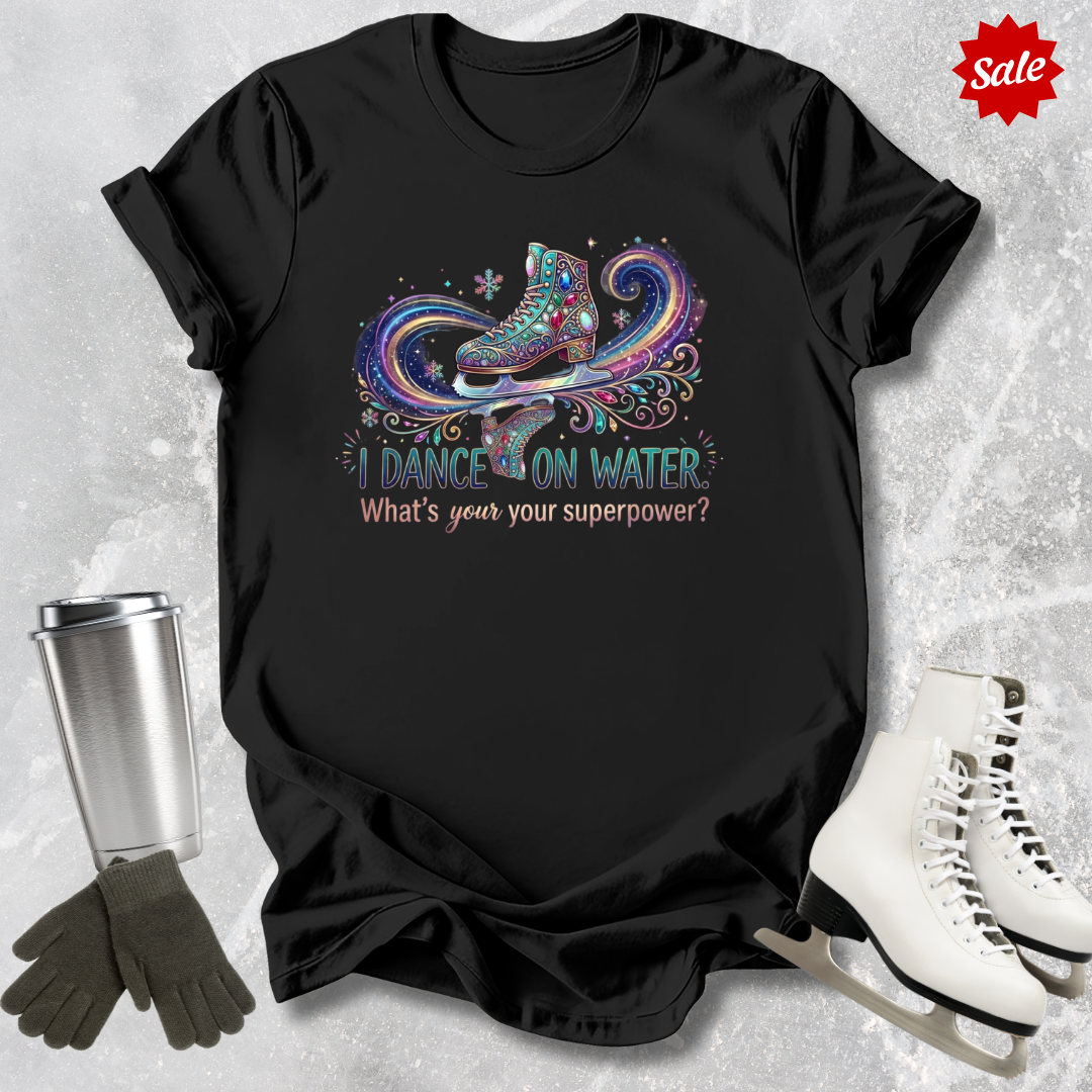 Black t-shirt with ice skating I dance on water design and text, surrounded by ice skates and a tumbler on a textured gray background.