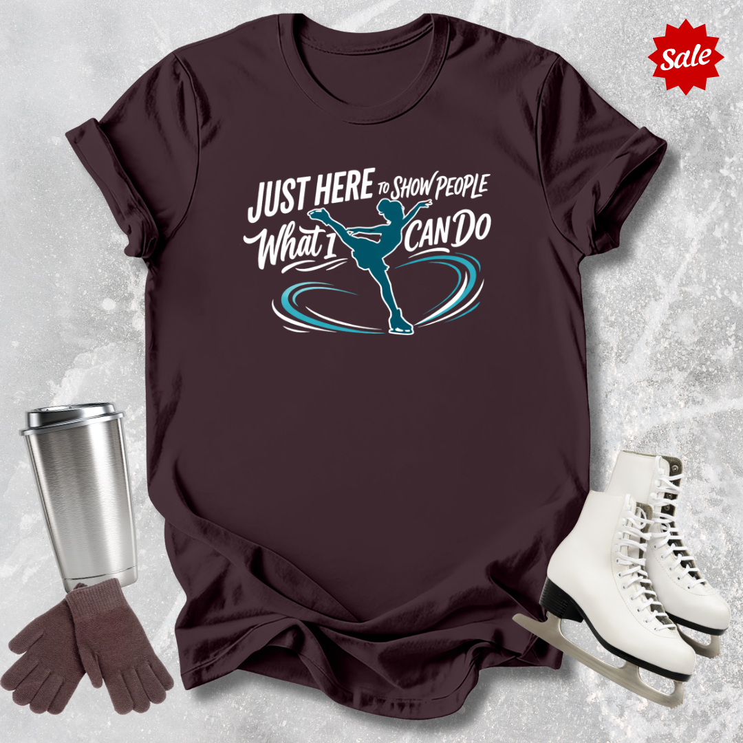 Brown t-shirt with just here to show people what I can do figure skating graphic design and accessories on a textured surface