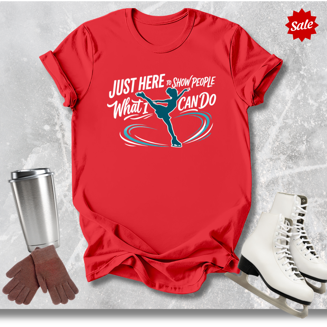 Red t-shirt with just here to show people what I can do figure skating motivational graphic, white skates, silver tumbler, and brown gloves on a textured gray background.