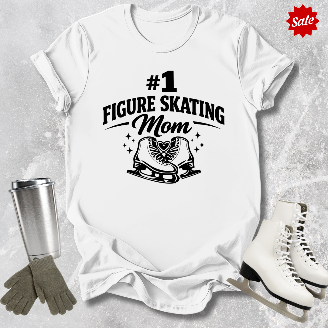 White t-shirt with '#1 Figure Skating Mom' design, surrounded by ice skates, gloves, and a tumbler on a textured surface.