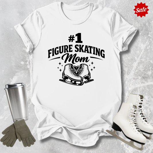 White t-shirt with '#1 Figure Skating Mom' design, surrounded by ice skates, gloves, and a tumbler on a textured surface.