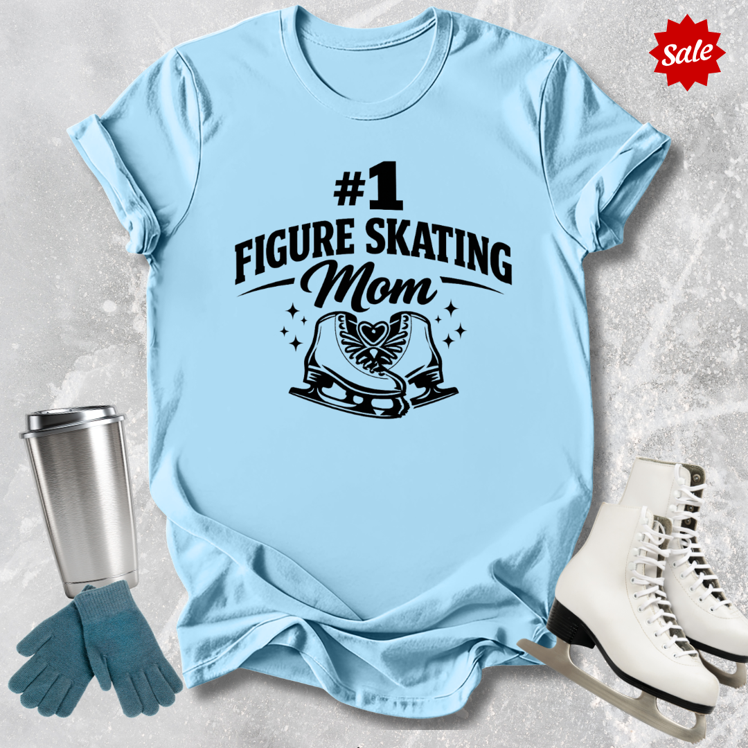 Light blue t-shirt with '#1 Figure Skating Mom' text, surrounded by ice skates and a tumbler on a textured surface.