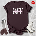 Maroon t-shirt with 'SKATER INTERMEDIATE' text, silver tumbler, brown gloves, and white skates on a textured gray background.