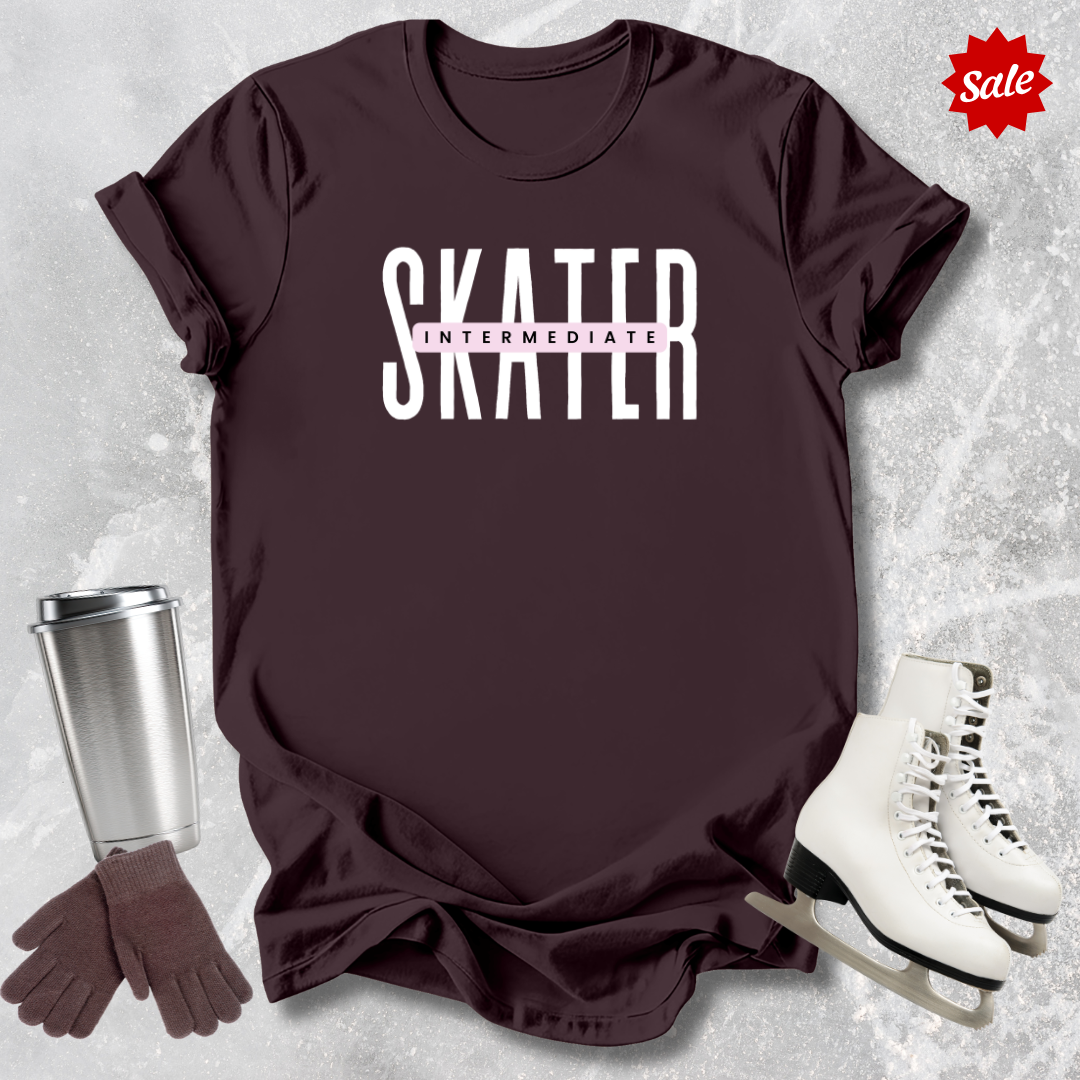 Maroon t-shirt with 'SKATER INTERMEDIATE' text, silver tumbler, brown gloves, and white skates on a textured gray background.