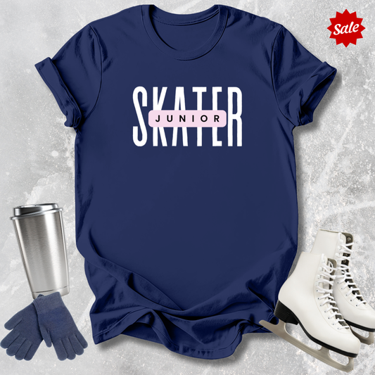 Navy blue t-shirt with 'SKATER JUNIOR' text, silver tumbler, gloves, and ice skates on a textured gray background.