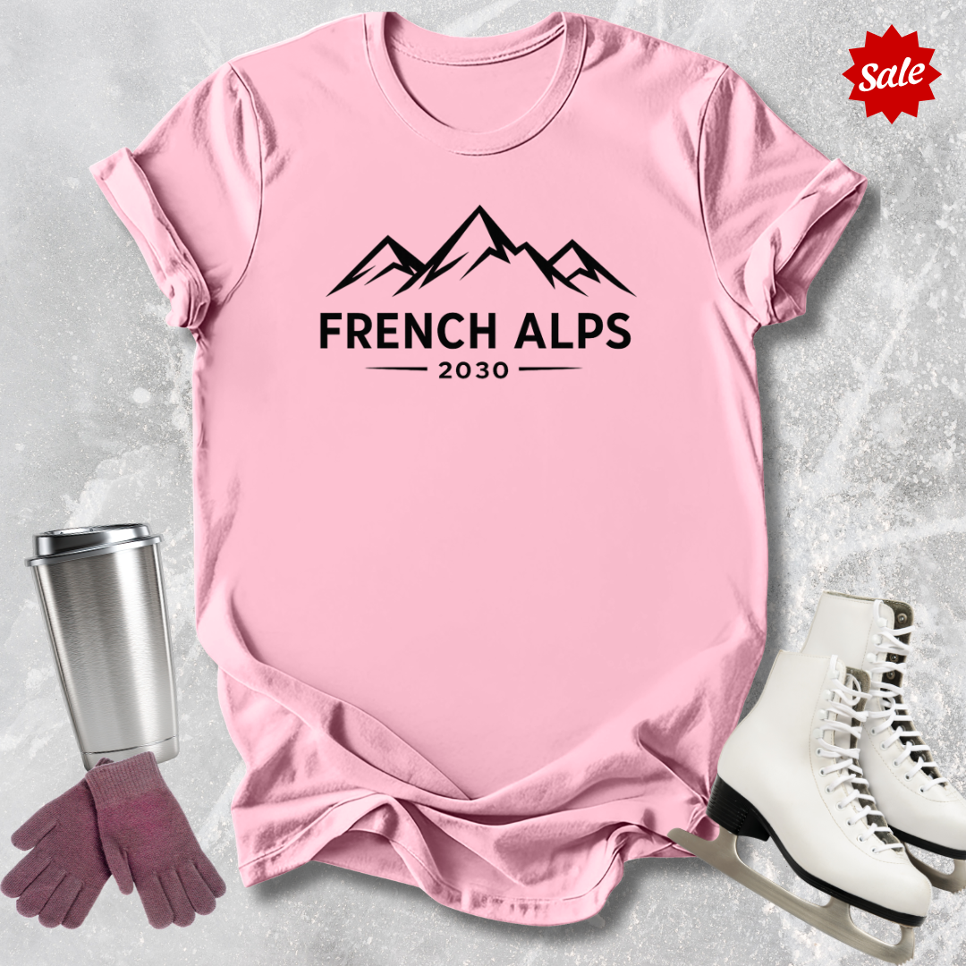 Pink t-shirt with 'French Alps 2030' text and graphics, surrounded by a silver tumbler, pink gloves, and white skates on a light gray background.