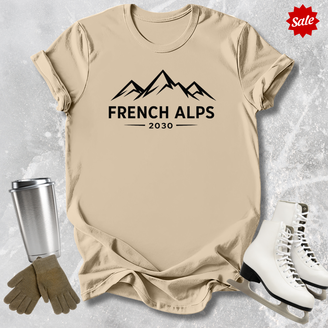 Beige t-shirt with 'French Alps 2030' text, silver tumbler, brown gloves, and white skates on a light gray background.