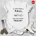 White t-shirt with humorous  if you didn't fall did you even train text, silver tumbler, gray gloves, and white ice skates on a textured surface.