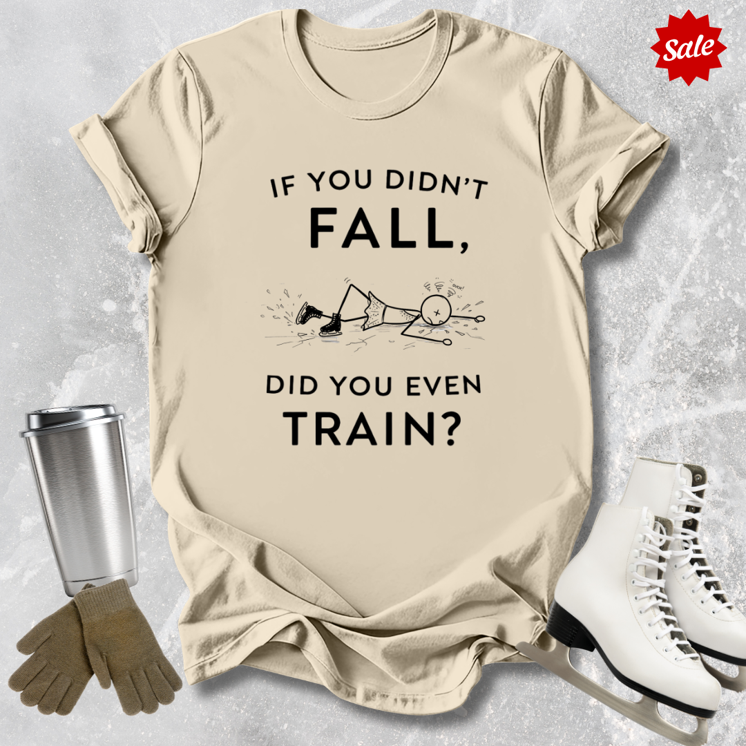 Beige t-shirt with humorous  if you didn't fall did you even train text, and graphics, placed on a textured surface with ice skates and a tumbler.