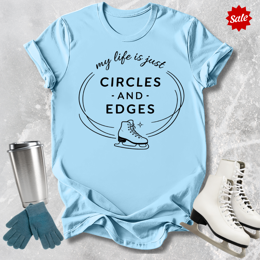 Light blue t-shirt with 'my life is just circles and edges' text and ice skate graphic, surrounded by ice skates and gloves on a textured surface.