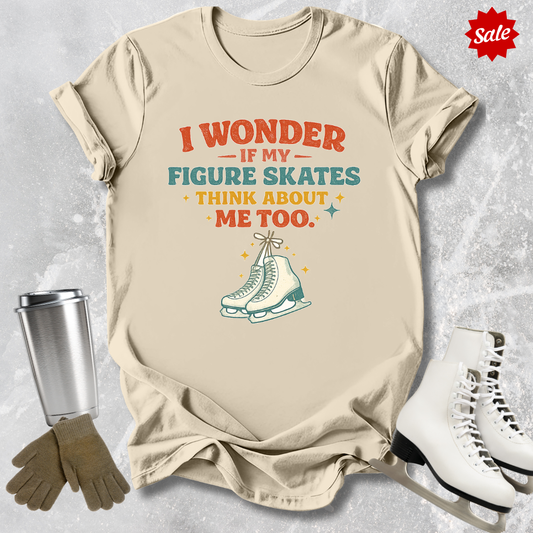 Beige t-shirt with figure skating graphic and text, surrounded by ice skates and gloves on a textured surface.