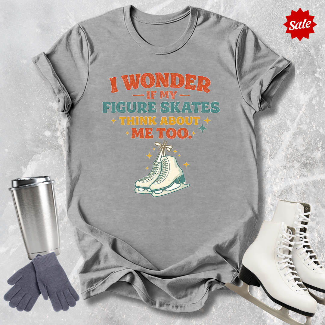 Gray t-shirt with humorous figure skating graphic and text, surrounded by ice skates, gloves, and a tumbler on a textured gray background.