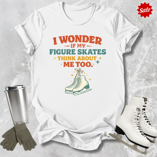 White t-shirt with humorous figure skating graphic and text, surrounded by ice skates and a tumbler on a textured surface.