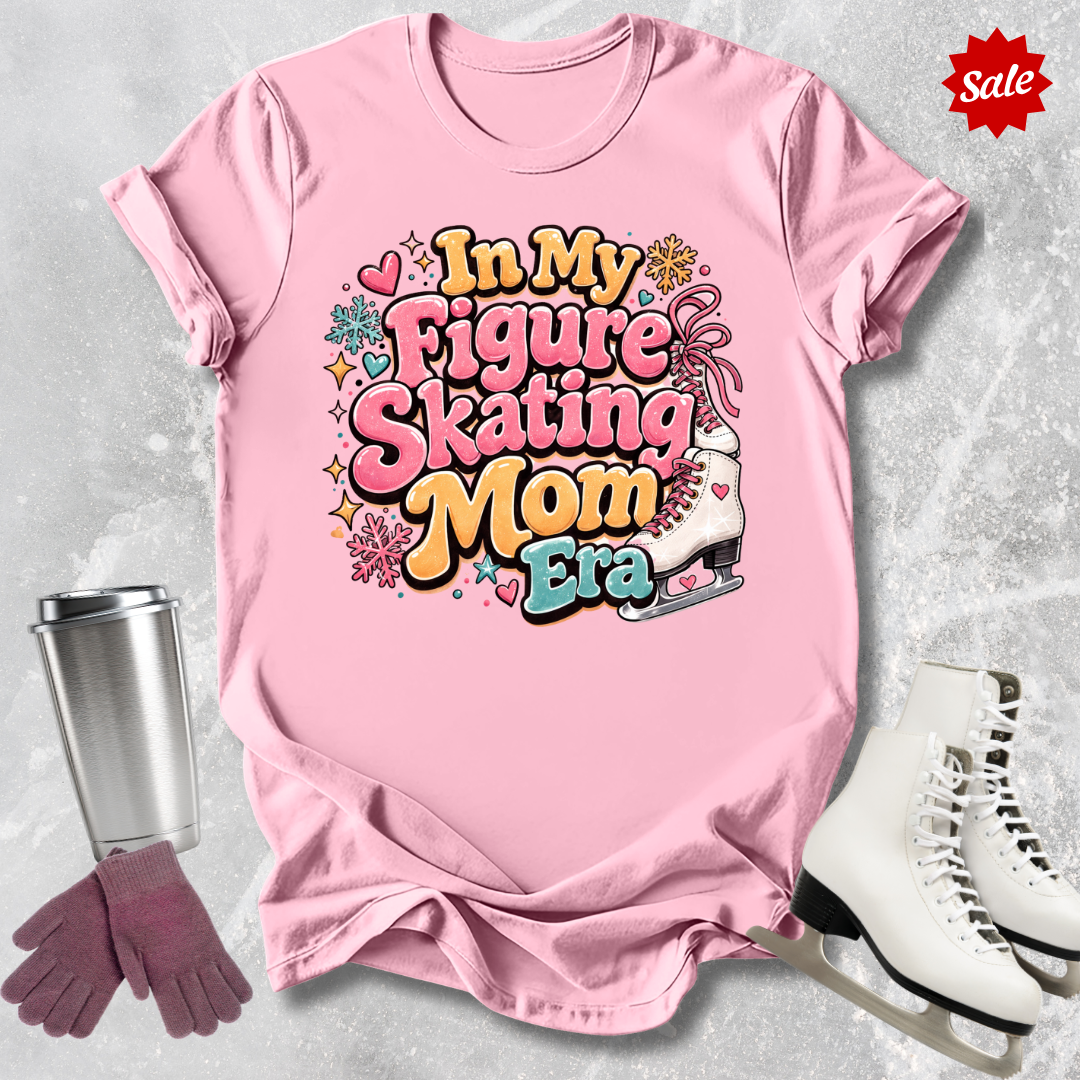 Pink t-shirt with figure skating-themed text, surrounded by ice skates and a tumbler on a light gray background.