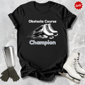 Black t-shirt with 'Obstacle Course Champion' text and ice skates, surrounded by ice skates and a tumbler on a textured gray background.