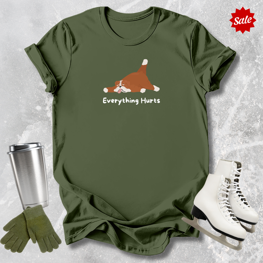 Green t-shirt with a cartoon dog and 'Everything Hurts' text, displayed with a tumbler, gloves, and skates on a textured gray background.