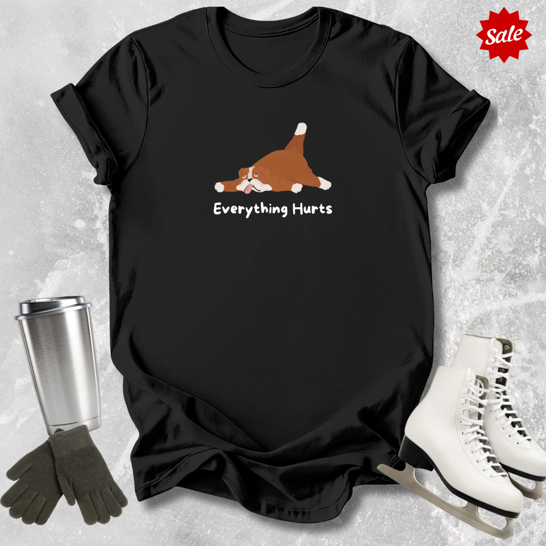 Black t-shirt with a dog graphic and 'Everything Hurts' text, surrounded by winter accessories on a textured surface.