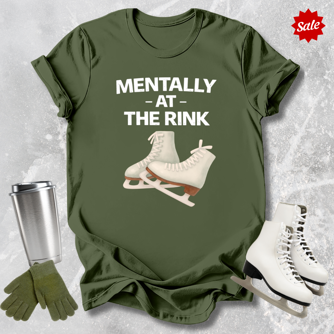Green t-shirt with ice skates and text 'Mentally at the Rink' on a textured gray background.