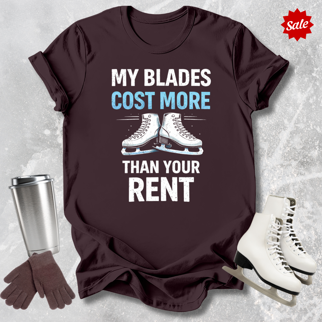 Brown t-shirt with 'MY BLADES COST MORE THAN YOUR RENT' text, next to a silver tumbler, black gloves, and white figure skates on a textured gray background.