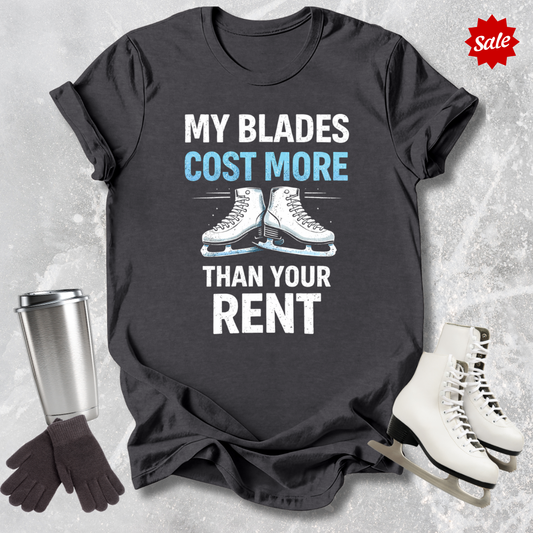 Gray t-shirt with 'MY BLADES COST MORE THAN YOUR RENT' text, next to a silver tumbler, black gloves, and white figure skates on a textured gray background.